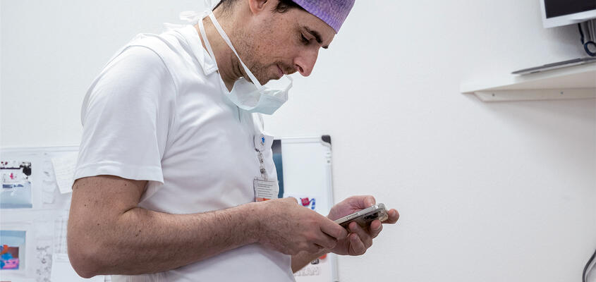 Arzt in mit Maske schaut auf Smartphone