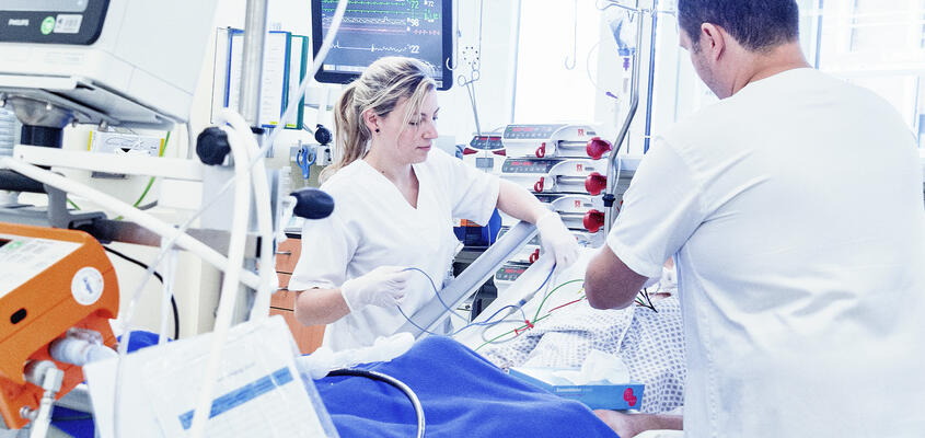 Zwei Pflegefachpersonen kümmern sich um einen Patienten auf der intensivstation.